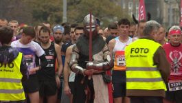 Uczestnicy Biegu Niepodległości stoją na linii startu, wśród nich osoba przebrana za rycerza w zbroi z mieczem, symbolicznie nawiązująca do historii Polski. W tle widać biegaczy w sportowych strojach i fotografów w kamizelkach odblaskowych, gotowych do uwiecznienia momentu rozpoczęcia biegu upamiętniającego 11 listopada (fot. TVP SPORT)