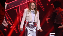 Ola Antoniak ubrana w beżowo-srebrny strój na scenie. W tle czerwień. Dziewczyna trzyma mikrofon.
