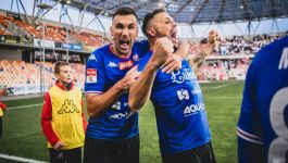 Na zdjęciu widzimy eksplozję radości piłkarzy Podbeskidzia Bielsko-Biała po efektownym zwycięstwie w niedzielnym meczu Betclic 2 Ligi. Dwaj zawodnicy w niebieskich koszulkach, z widocznymi logotypami sponsorów „Betclic”, „Lukosz”, „AQUA” i „Bielsko-Biała”, świętują zdobycie bramki — jeden z nich obejmuje drugiego, obaj krzyczą z euforią, wyrażając czystą, nieskrępowaną radość (fot. TS Podbeskidzie/Szymon Jaszczurowski)