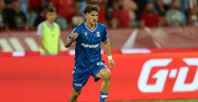 Pablo Rodriguez (fot. Getty Images) Pablo Rodriguez, hiszpański piłkarz Lecha Poznań, w niebieskiej koszulce klubowej z wyraźnym logo "SUPERBET" na środku, biegnie z piłką na boisku podczas meczu. Ma kręcone, brązowe włosy, intensywne spojrzenie i opaskę na lewym nadgarstku. Na pierwszym planie widać jego muskularne nogi i białe buty sportowe. W tle, za czerwoną bandą reklamową z logo "G-D", widać niewyraźne sylwetki kibiców na trybunach.